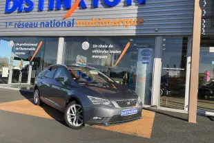 SEAT LEON ST gris en 3/4 avant droit, garée devant un showroom avec plaques Distinxion visibles.
