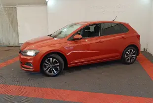 Volkswagen Polo 1.0 TSI orange vue de profil côté gauche, phares allumés, jantes alliage noires et argentées.