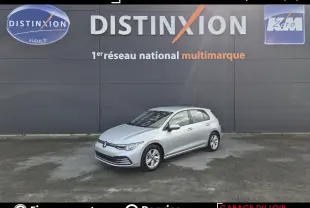 Volkswagen Golf gris clair vue 3/4 avant droit, stationnée devant un mur gris avec logo Distinxion.