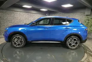 Profil latéral gauche de l'Alfa Romeo Tonale 1.3 PHEV bleu métallisé avec rétroviseurs noirs brillants en intérieur.