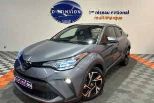 Toyota C-HR hybride gris célestine vu en 3/4 avant droit avec phares LED allumés et jantes noires bicolores.