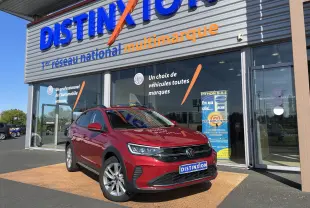 Volkswagen Taigo rouge roi en 3/4 avant droit devant un showroom Distinxion, avec jantes alliage et calandre noire.