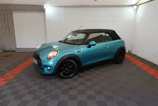 Vue 3/4 avant d'une MINI One cabriolet bleu avec capote noire et jantes noires dans un garage.