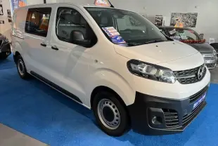 Vue 3/4 avant droit d'un Opel Vivaro Fourgon blanc exposé en showroom avec marquage publicitaire sur pare-brise.