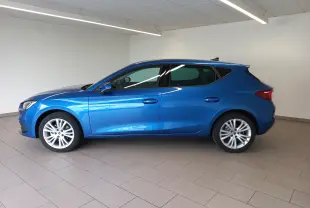 Vue de profil côté gauche d'une SEAT Leon 2025 bleu saphir aux vitres arrière surteintées dans un intérieur lumineux.