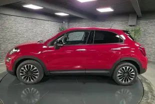 Profil droit d'un Fiat 500X rouge Passione 2024 avec jantes alliage 17'' et vitres surteintées en intérieur showroom.