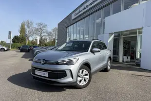 Volkswagen Tiguan gris en 3/4 avant droit devant un concessionnaire, avec jantes alliage et calandre noire.