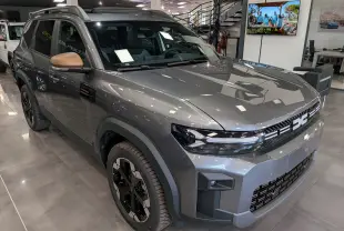 SUV Dacia Bigster Hybrid-G 150 4x4 gris schiste vu en 3/4 avant droit avec rétroviseurs bronze et jantes noires.