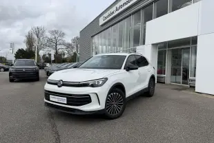 Volkswagen Tiguan blanc vu en 3/4 avant droit, avec jantes noires et calandre noire brillante, devant un concessionnaire.