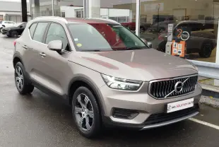 Vue 3/4 avant droit d'un Volvo XC40 beige 2020 avec calandre verticale et jantes bi-ton, stationné devant un showroom.