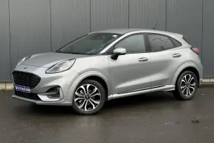 Vue 3/4 avant droit d'un Ford Puma gris Solar avec jantes alliage et vitres surteintées, garé devant un mur gris.