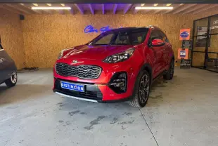 KIA Sportage 1.6 CRDI rouge en 3/4 avant droit, avec calandre noire et jantes alliage visibles en intérieur showroom.