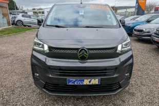 Vue frontale d'un Citroën Jumpy gris avec phares LED allumés et plaque Zéro KM sur un parking.