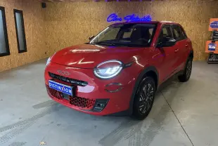 Vue 3/4 avant d'une FIAT 600 rouge 2024 avec phares allumés, calandre noire et jantes stylisées en intérieur bois.