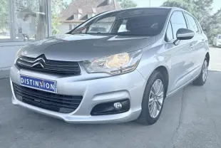 Citroën C4 gris vue 3/4 avant droit avec phares allumés et jantes alliage, stationnée devant un bâtiment.