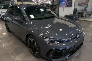 Vue 3/4 avant droite d'une Volkswagen Golf VIII 1.5 eTSI R-Line gris Urano avec jantes noires biton visibles en showroom.