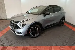 KIA Sportage gris clair en 3/4 avant droit, avec calandre noire et jantes noires à motifs géométriques.