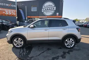 Profil côté gauche d'un Volkswagen T-Cross gris métallisé 2025 avec jantes alliage 17 pouces, stationné devant un garage.