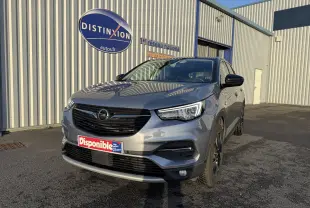 Opel Grandland X gris quartz en 3/4 avant droit, avec calandre noire et jantes foncées, stationné devant un bâtiment industriel.
