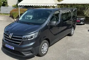 Vue 3/4 avant droit d'un Renault Trafic Combi gris comète, avec calandre chromée et phares LED distinctifs.