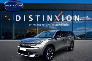 Citroën C4 X gris mercure en 3/4 avant droit, avec jantes alu et calandre distinctive, devant un showroom Distinxion.