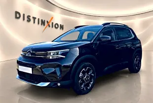 Citroën C5 Aircross noir en 3/4 avant droit, avec barres de toit et jantes alu distinctives dans un showroom lumineux.