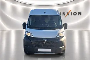 Vue de face du Peugeot Boxer Fourgon blanc avec large calandre noire et phares allumés dans un studio lumineux.
