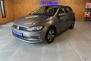 Volkswagen Polo 1.0 TSI gris vue 3/4 avant droit dans un showroom avec éclairage intérieur et logo néon bleu.