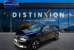 Vue 3/4 avant droite de la Citroën C4 X noire 2025 avec jantes alu et phares LED devant un showroom Distinxion.