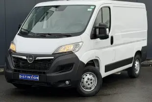 Vue 3/4 avant droit d’un Opel Movano Fourgon blanc avec calandre noire et feux allumés sur sol humide.