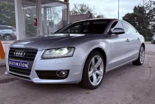 Audi A5 gris vue 3/4 avant droit avec phares allumés et jantes alliage cinq branches.