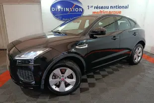 Jaguar E-PACE noir en 3/4 avant droit, avec jantes argentées et phares LED allumés en intérieur showroom.