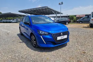 Peugeot 208 bleu Vertigo vue 3/4 avant droit sur parking, calandre noire avec logo lion et phares LED distinctifs.