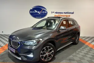 BMW X1 gris en vue 3/4 avant droit, avec toit ouvrant et jantes alliage distinctives, dans un showroom lumineux.