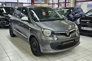 Renault Twingo III gris lunaire vue 3/4 avant droit en intérieur, avec rétroviseurs blancs et jantes acier noires.