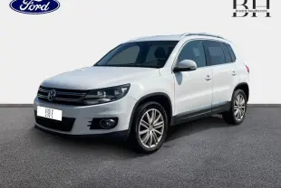 Volkswagen Tiguan blanc Candy en 3/4 avant droit, avec jantes alliage et barres de toit visibles.