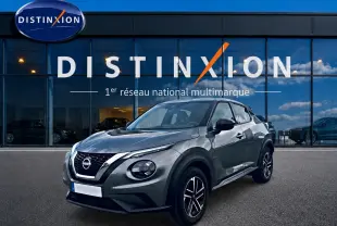 Nissan Juke gris 2025 en 3/4 avant droit, avec jantes alu et calandre noire brillante devant showroom Distinxion.