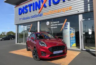 Ford Puma rouge vue 3/4 avant droit, garée devant un showroom avec logo Distinxion en arrière-plan.