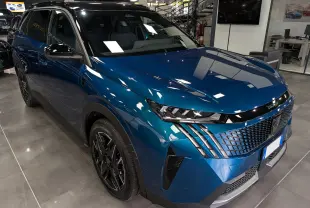 Vue 3/4 avant droit du Peugeot 5008 Hybrid bleu Obsession avec toit noir et jantes noires en concession.