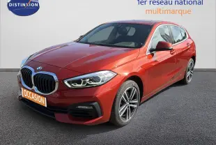 BMW Série 1 116i Business orange Sunset vue 3/4 avant droit, avec calandre imposante et jantes alliage bicolores.