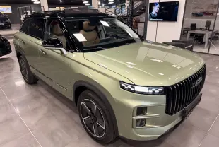 Vue 3/4 avant d’un SUV JAECOO J7 hybride rechargeable gris olive avec toit noir et intérieur cuir brun en showroom.