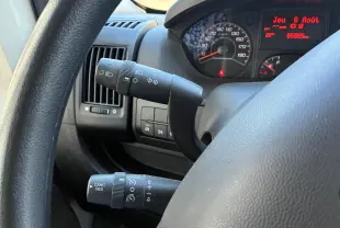 Gros plan sur le volant et les commandes du tableau de bord du Peugeot Boxer cabine approfondie gris, avec compteur et affichage digital rouge.