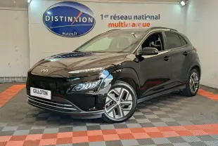Hyundai Kona électrique noir en 3/4 avant droit, avec jantes spécifiques et feux LED allumés en intérieur showroom.