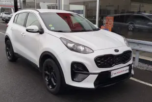 KIA Sportage blanc vue 3/4 avant droit avec calandre noire et jantes noires, stationné devant un showroom.