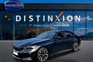 BMW Série 5 i5 M60 noir vue 3/4 avant avec jantes alu bicolores devant un showroom Distinxion.