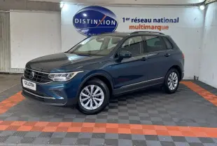 Volkswagen Tiguan bleu en 3/4 avant droit avec rails de toit noirs, stationné sur sol à damiers gris et orange.
