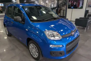 Vue 3/4 avant droite d'une Fiat Panda 1.0 Hybrid City bleu Italia en showroom avec détails noirs sur les rétroviseurs.