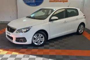 Peugeot 308 blanche vue de trois quarts avant droit, avec jantes alliage et phares allumés en intérieur showroom.