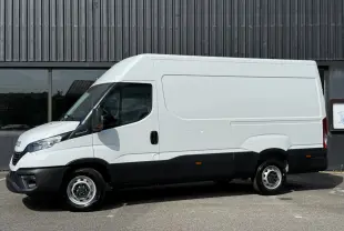 Vue de profil côté gauche d’un utilitaire Iveco Daily blanc avec bas de caisse noir, stationné devant un bâtiment industriel.