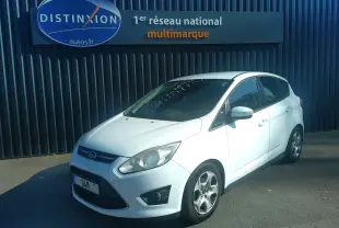 Ford C-MAX blanc vue 3/4 avant droit, garé devant un mur noir avec enseigne Distinxion.